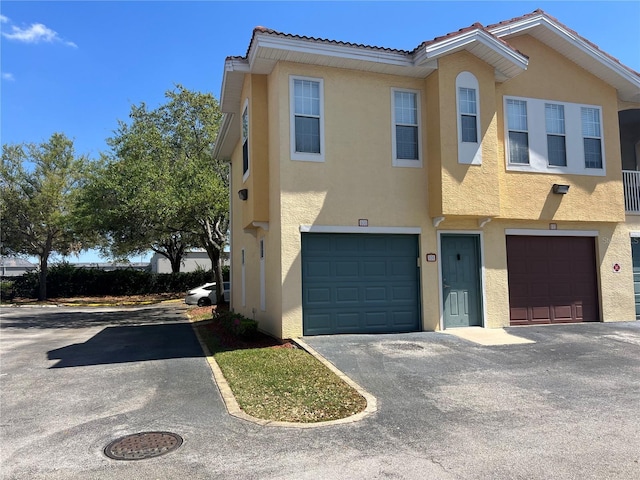 view of property with stucco siding, an attached garage, driveway, and a tiled roof