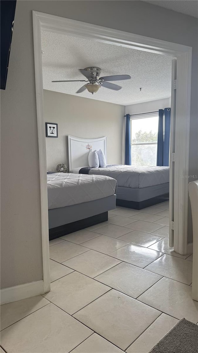 unfurnished bedroom featuring light tile patterned floors, baseboards, a ceiling fan, and a textured ceiling