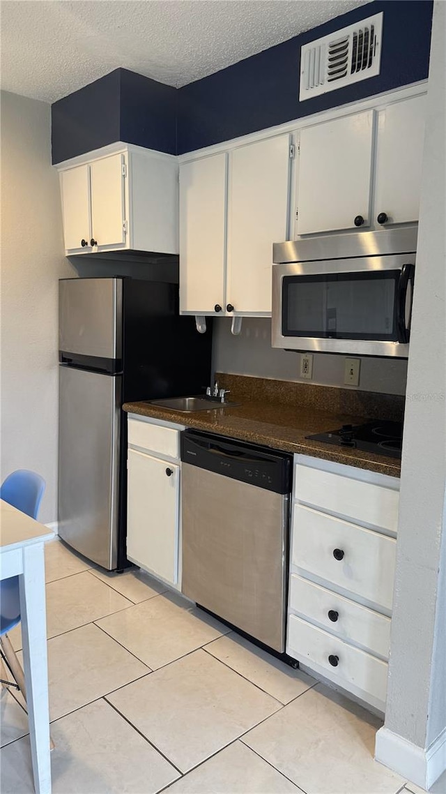 kitchen featuring stainless steel appliances, dark countertops, visible vents, white cabinets, and a textured ceiling