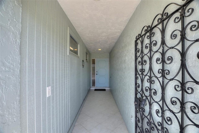 hallway featuring light tile patterned flooring, a textured ceiling, and a textured wall