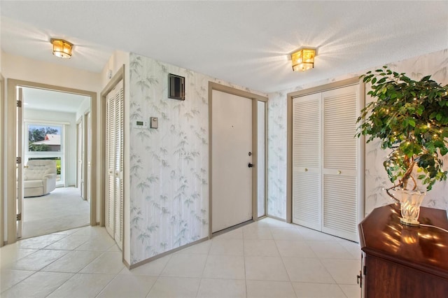 foyer entrance featuring light tile patterned floors, a textured ceiling, baseboards, and wallpapered walls