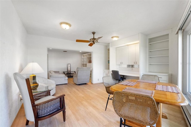 office with light wood finished floors, ceiling fan, built in shelves, and built in desk