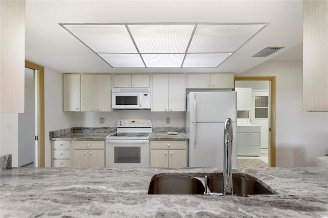 kitchen with white appliances, washer / clothes dryer, light stone counters, cream cabinets, and a sink