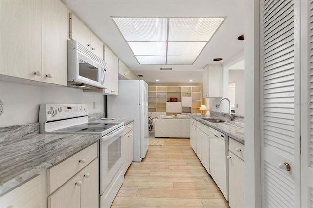 kitchen with light stone counters, open floor plan, a sink, light wood-type flooring, and white appliances