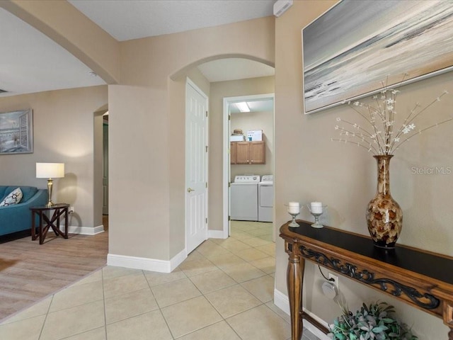 hallway featuring arched walkways, light tile patterned floors, and washing machine and dryer