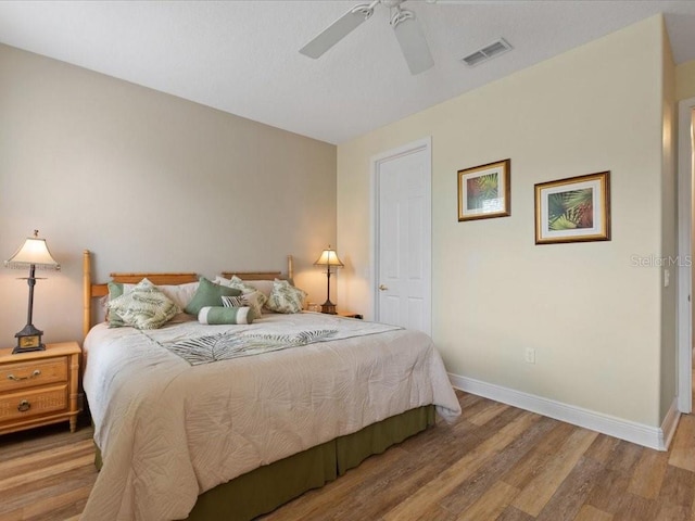 bedroom featuring ceiling fan, visible vents, baseboards, and wood finished floors