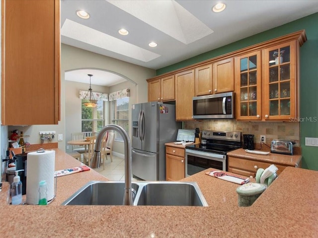 kitchen featuring backsplash, glass insert cabinets, light countertops, stainless steel appliances, and a sink