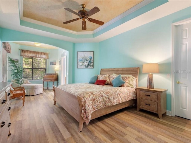 bedroom featuring a tray ceiling, arched walkways, wood finished floors, and crown molding