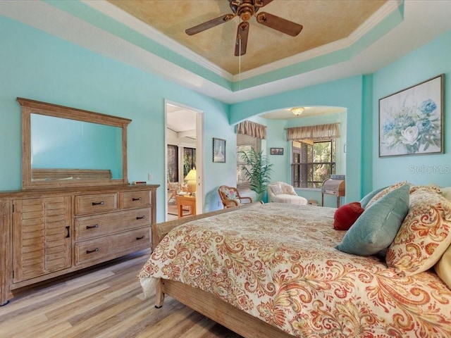 bedroom with a tray ceiling, ensuite bathroom, light wood-style floors, and crown molding