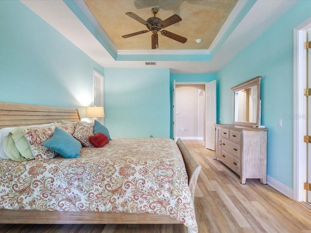 bedroom with visible vents, ornamental molding, wood finished floors, arched walkways, and a raised ceiling