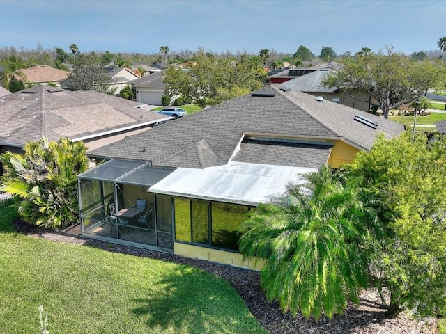 back of property featuring a lawn, roof with shingles, and a lanai