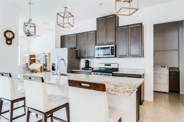 kitchen with a kitchen bar, a sink, appliances with stainless steel finishes, dark brown cabinets, and washer / dryer