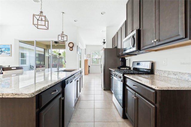 kitchen featuring dark brown cabinets, a center island with sink, light tile patterned floors, appliances with stainless steel finishes, and a sink