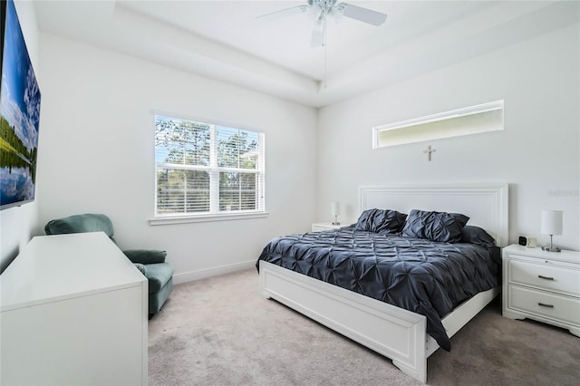 carpeted bedroom featuring a tray ceiling, baseboards, and a ceiling fan