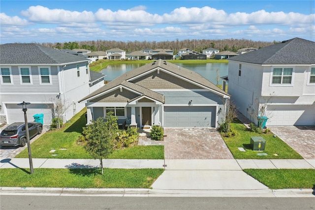 view of front of house featuring a water view, a residential view, decorative driveway, and a front yard