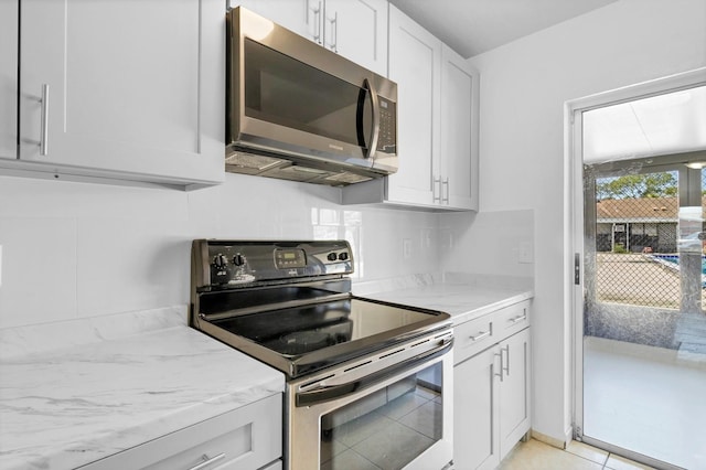 kitchen featuring stainless steel appliances, light stone counters, white cabinetry, and decorative backsplash