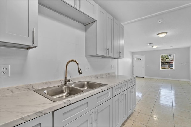 kitchen featuring light tile patterned floors, baseboards, light stone countertops, white cabinetry, and a sink