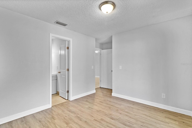 unfurnished bedroom featuring light wood finished floors, visible vents, connected bathroom, a textured ceiling, and baseboards