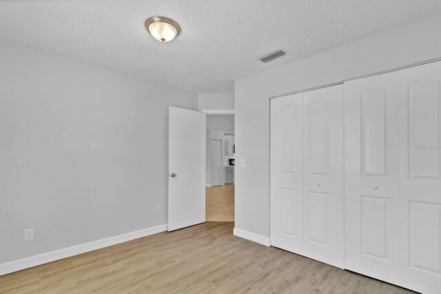 unfurnished bedroom with a textured ceiling, visible vents, baseboards, a closet, and light wood finished floors