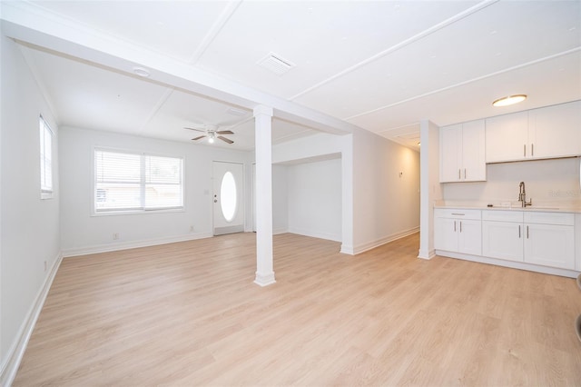 unfurnished living room with light wood finished floors, visible vents, a ceiling fan, a sink, and baseboards