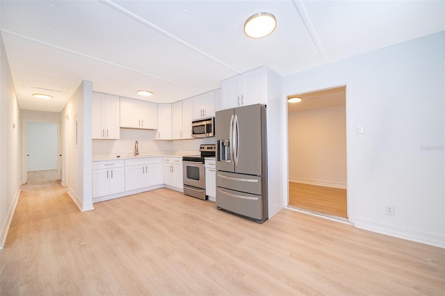 kitchen with stainless steel appliances, light countertops, white cabinets, a sink, and light wood-type flooring