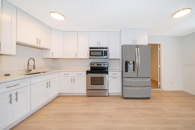 kitchen with white cabinets, light wood-style flooring, stainless steel appliances, and a sink