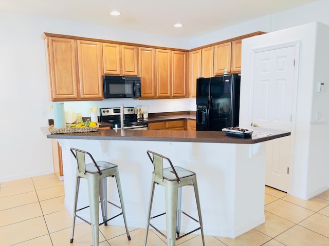 kitchen featuring light tile patterned floors, black appliances, a breakfast bar, and dark countertops