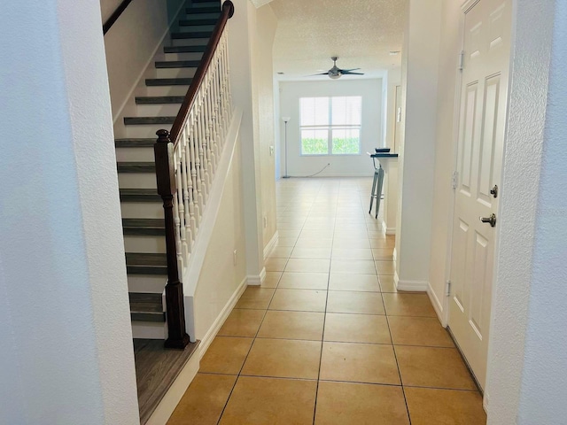 hallway featuring baseboards, a textured ceiling, and tile patterned floors