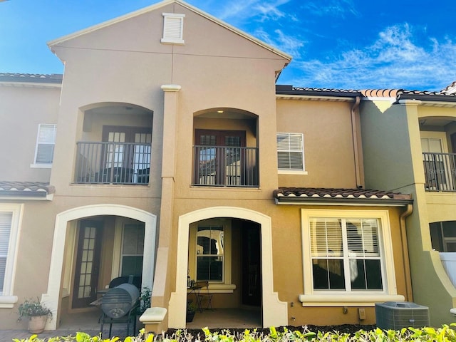 rear view of property featuring a tile roof, cooling unit, and stucco siding