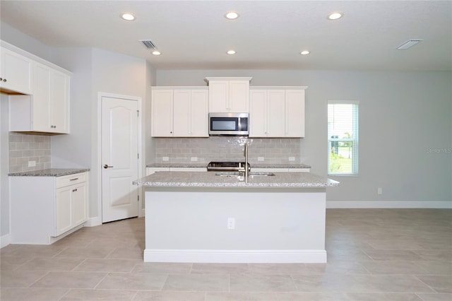 kitchen with visible vents, a kitchen island with sink, stainless steel microwave, and a sink