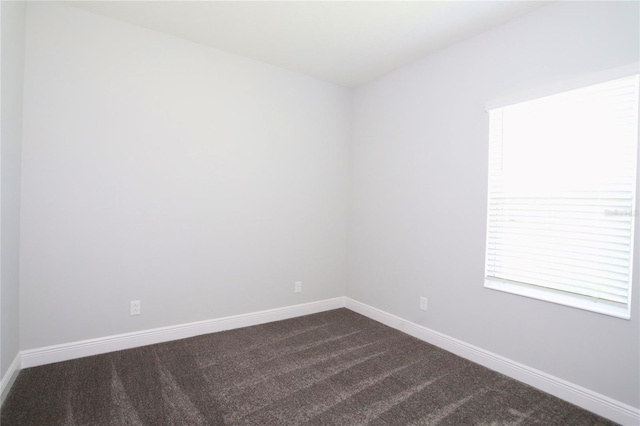 empty room featuring dark colored carpet and baseboards