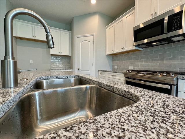 14552 Skipping Stone Loop, Parrish, FL 34219 - kitchen with white cabinets, light stone countertops, a sink, stainless steel appliances, and backsplash