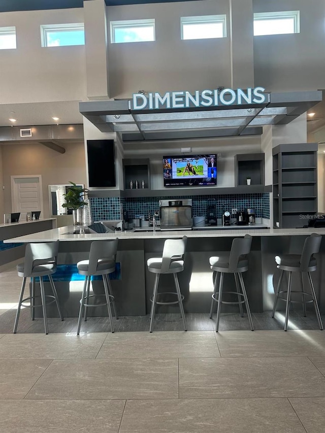 bar with tasteful backsplash, visible vents, a healthy amount of sunlight, and a high ceiling