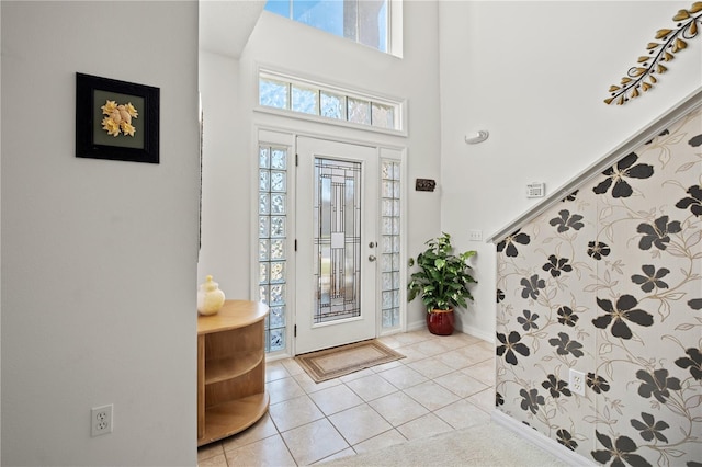 foyer entrance featuring a high ceiling, light tile patterned floors, and baseboards