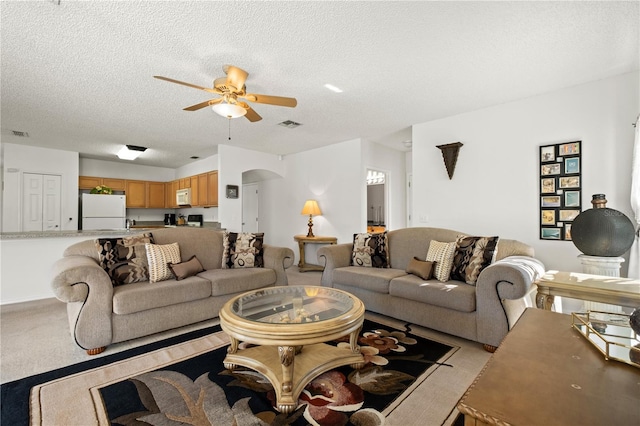 living area featuring a ceiling fan, visible vents, carpet floors, arched walkways, and a textured ceiling