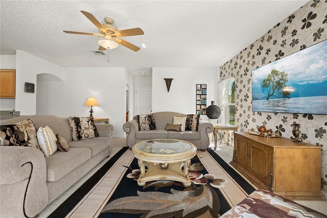 carpeted living area featuring a ceiling fan, visible vents, wallpapered walls, arched walkways, and a textured ceiling