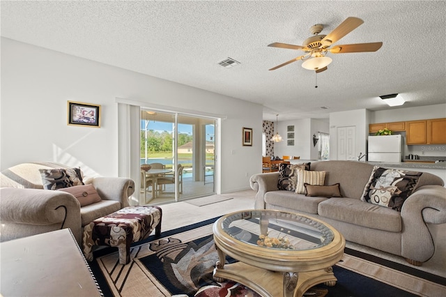 living area with a textured ceiling, light colored carpet, visible vents, and ceiling fan