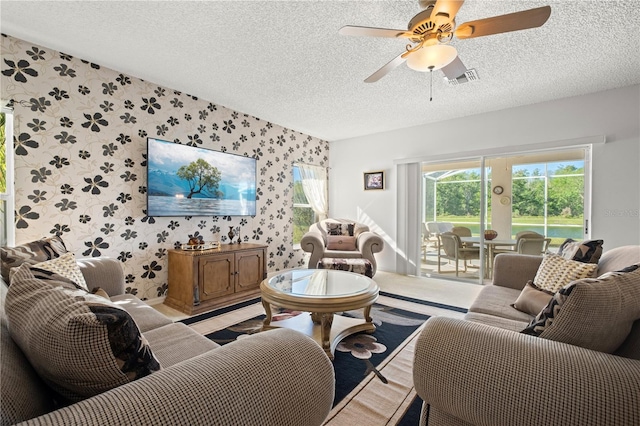 living area with wallpapered walls, ceiling fan, visible vents, and a textured ceiling