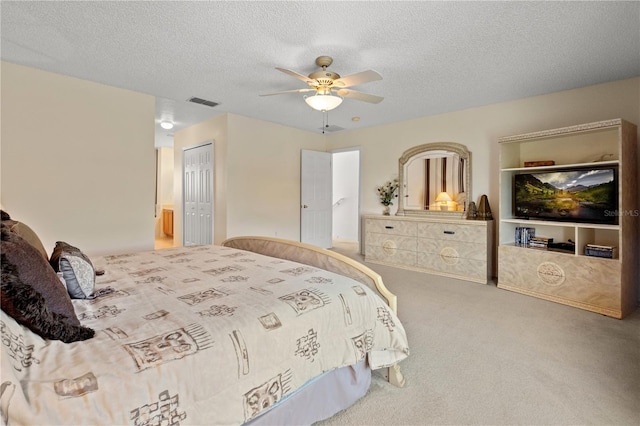 carpeted bedroom with a closet, visible vents, a textured ceiling, and ceiling fan