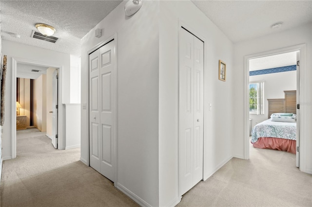 hallway featuring visible vents, light colored carpet, a textured ceiling, and baseboards