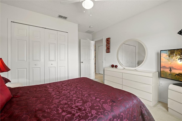 bedroom featuring light carpet, visible vents, a textured ceiling, and a closet