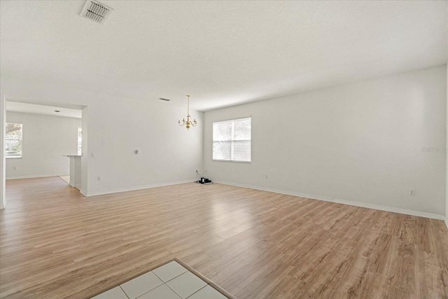 unfurnished living room featuring a notable chandelier, baseboards, visible vents, and light wood-style floors