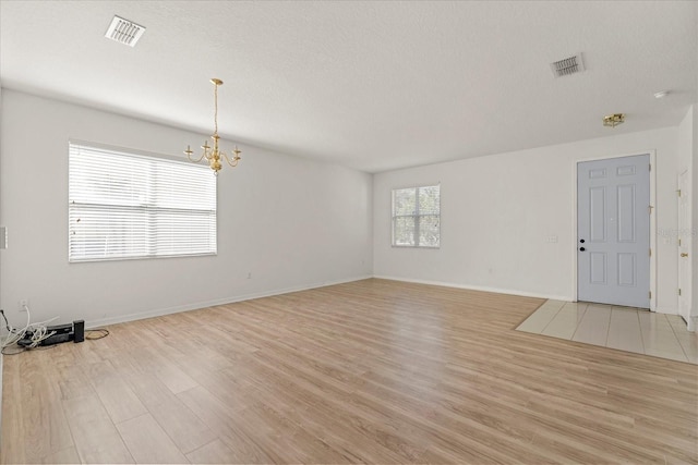 empty room featuring light wood-type flooring, baseboards, visible vents, and a notable chandelier