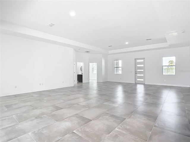 unfurnished living room with visible vents, recessed lighting, a raised ceiling, and baseboards