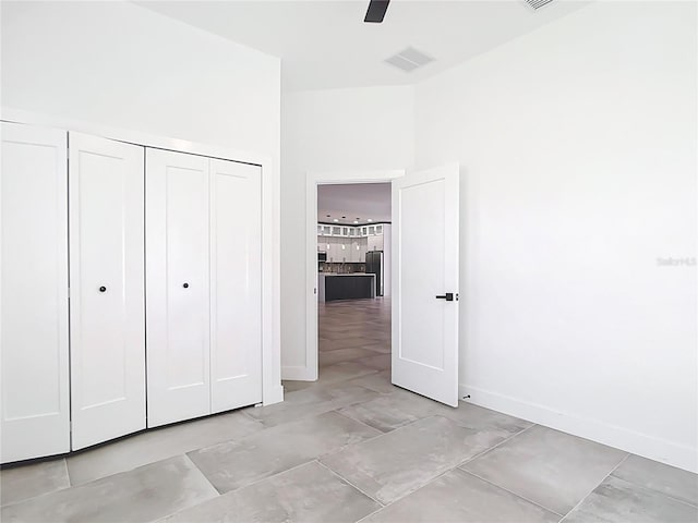 unfurnished bedroom with visible vents, ceiling fan, baseboards, freestanding refrigerator, and a closet