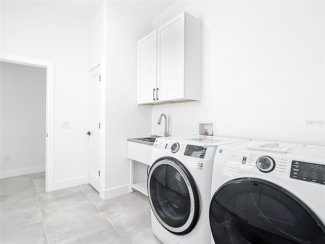 clothes washing area featuring washing machine and clothes dryer, cabinet space, and baseboards