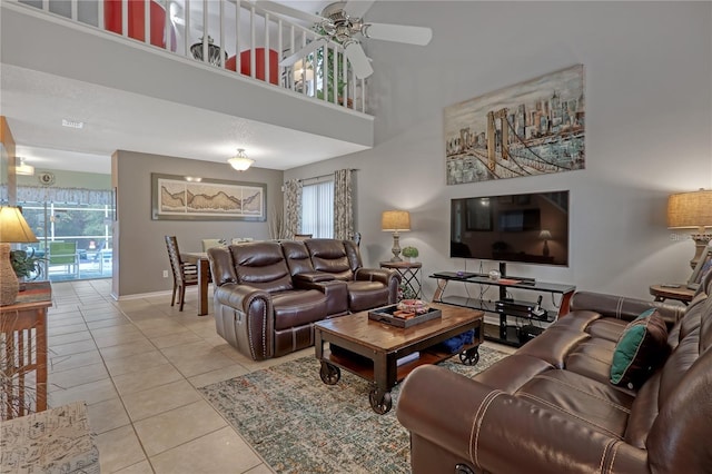 living area featuring light tile patterned floors, ceiling fan, a high ceiling, and baseboards