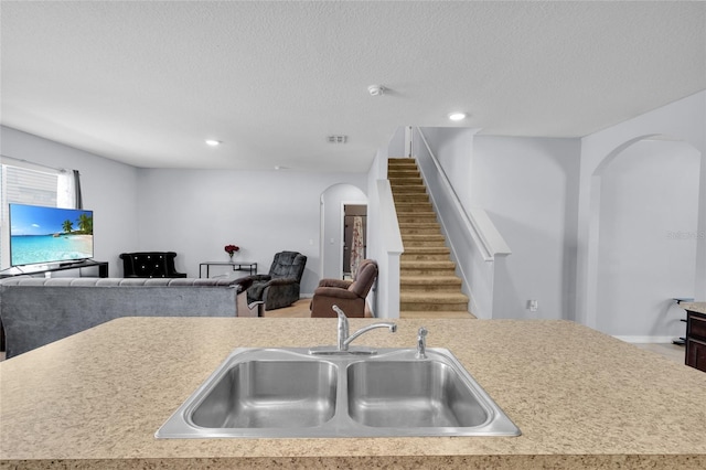 kitchen with a textured ceiling, light countertops, arched walkways, and a sink