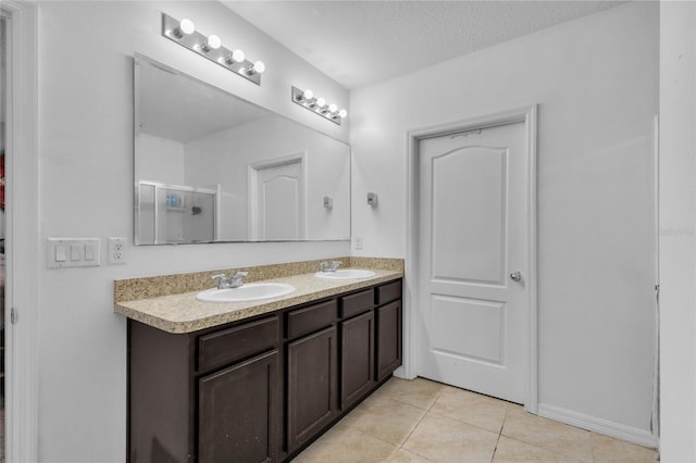 full bathroom featuring a shower with shower door, double vanity, a sink, tile patterned flooring, and a textured ceiling