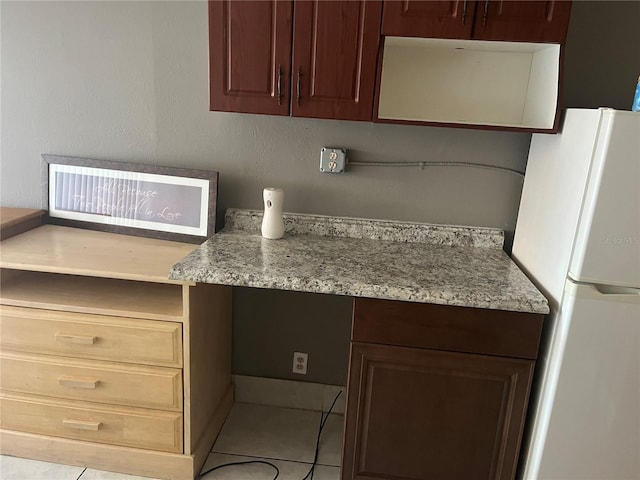 kitchen featuring built in desk, tile patterned flooring, freestanding refrigerator, and light stone countertops